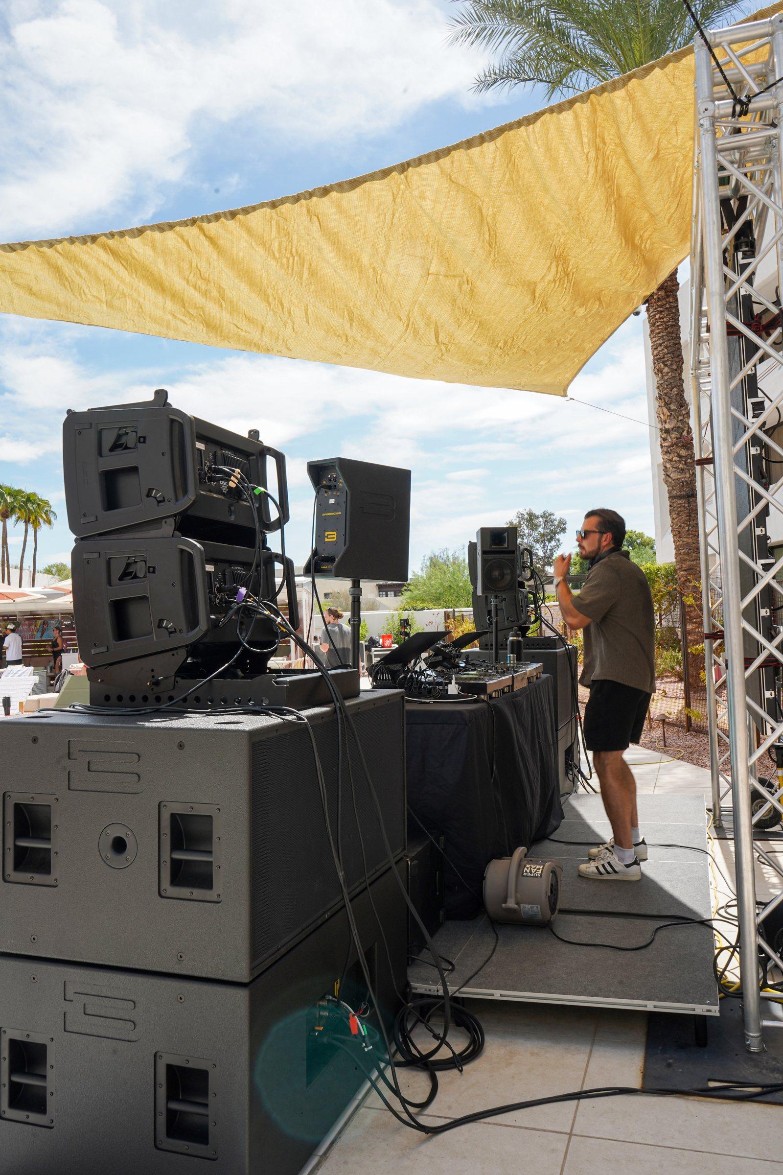 Two line array elements on a stack of subwoofers next to a DJ booth, with an engineer on stage